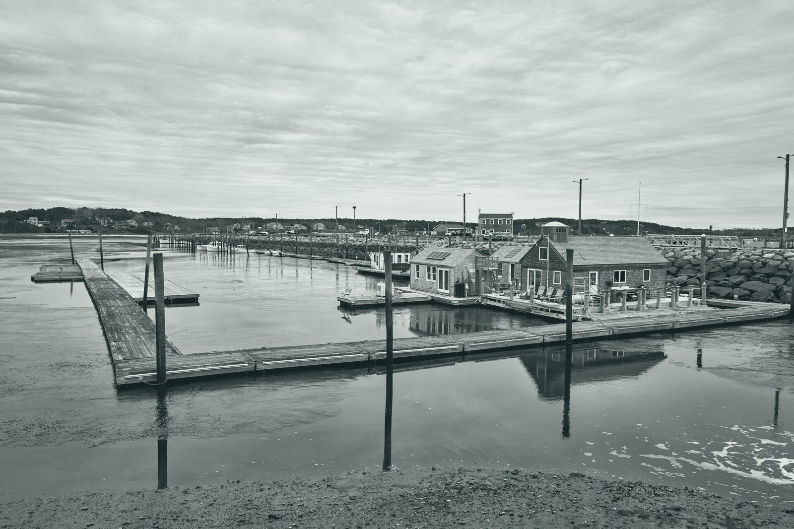 Wellfleet harbour: a wooden dock, moored boats and shingled sheds on the water under a grey sky