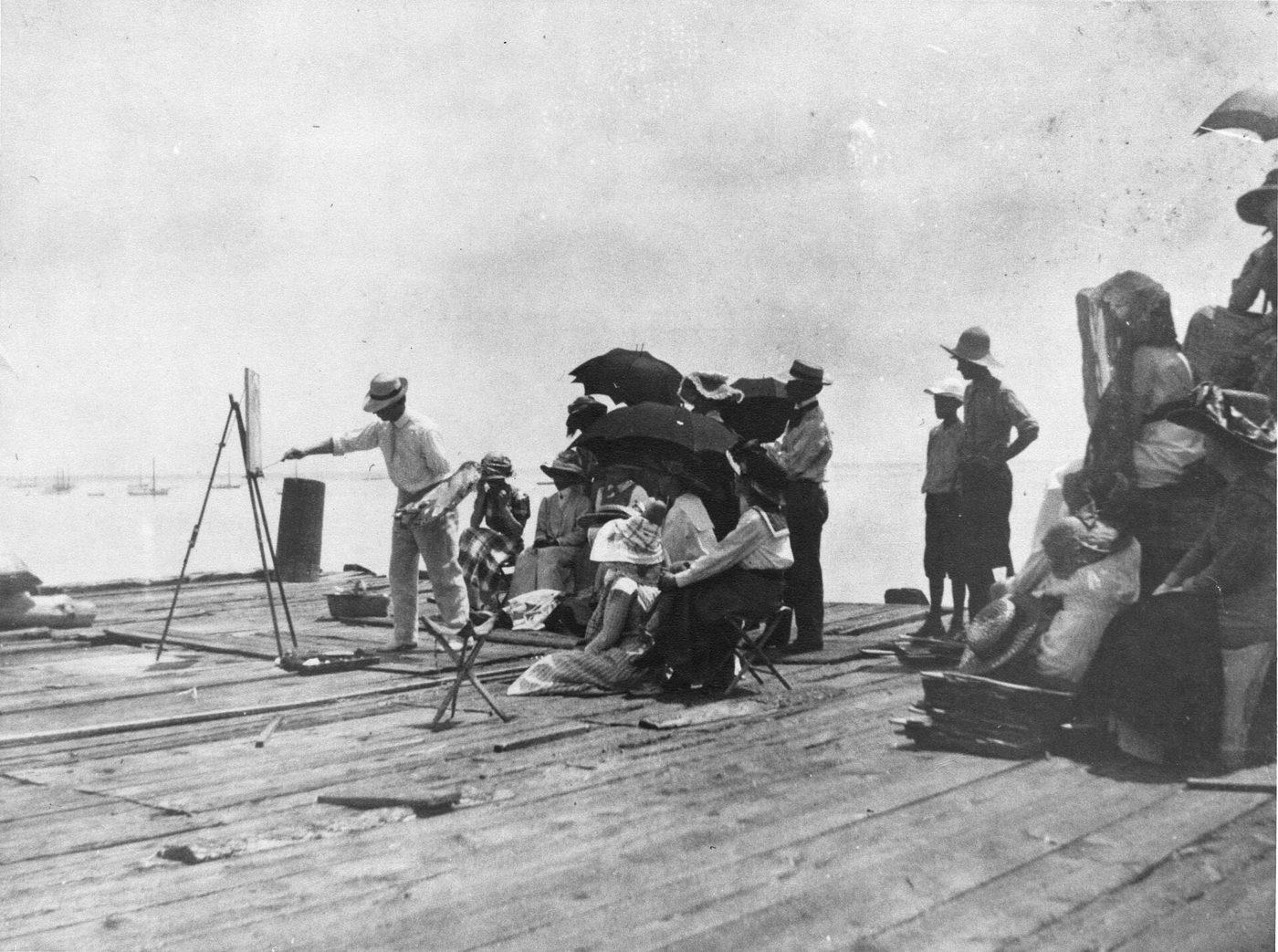 Archival photograph: Charles Webster Hawthorne demonstrating at an easel on a wharf while his painting class watches, about 1910.