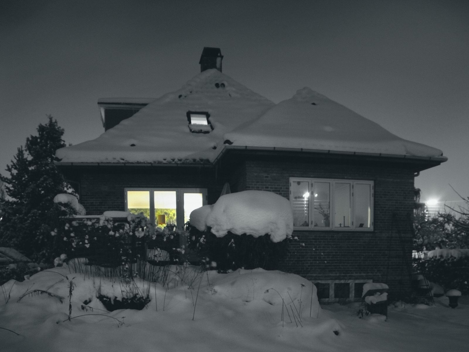 A brick house at night after snow, printed grey: two lit windows keep their warm colour.