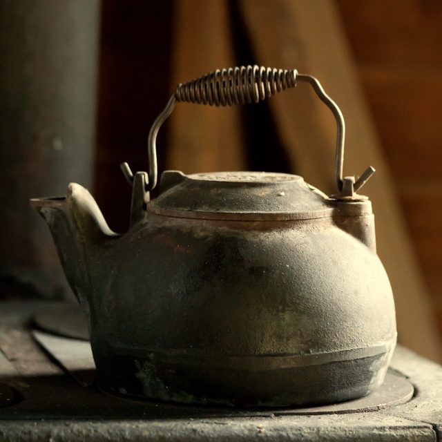 A cast-iron kettle on an old wood stove, in natural light.
